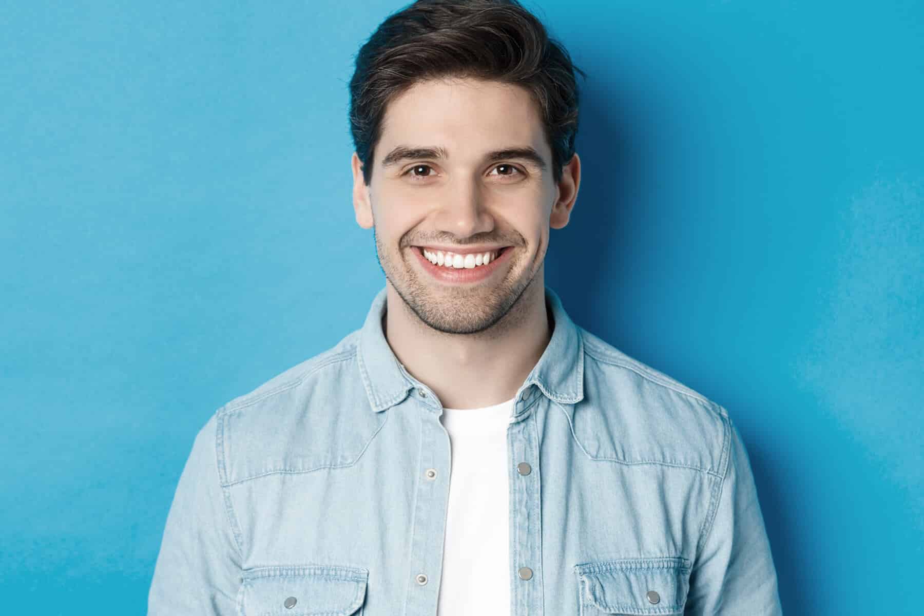 close up young successful man smiling camera standing casual outfit against blue background